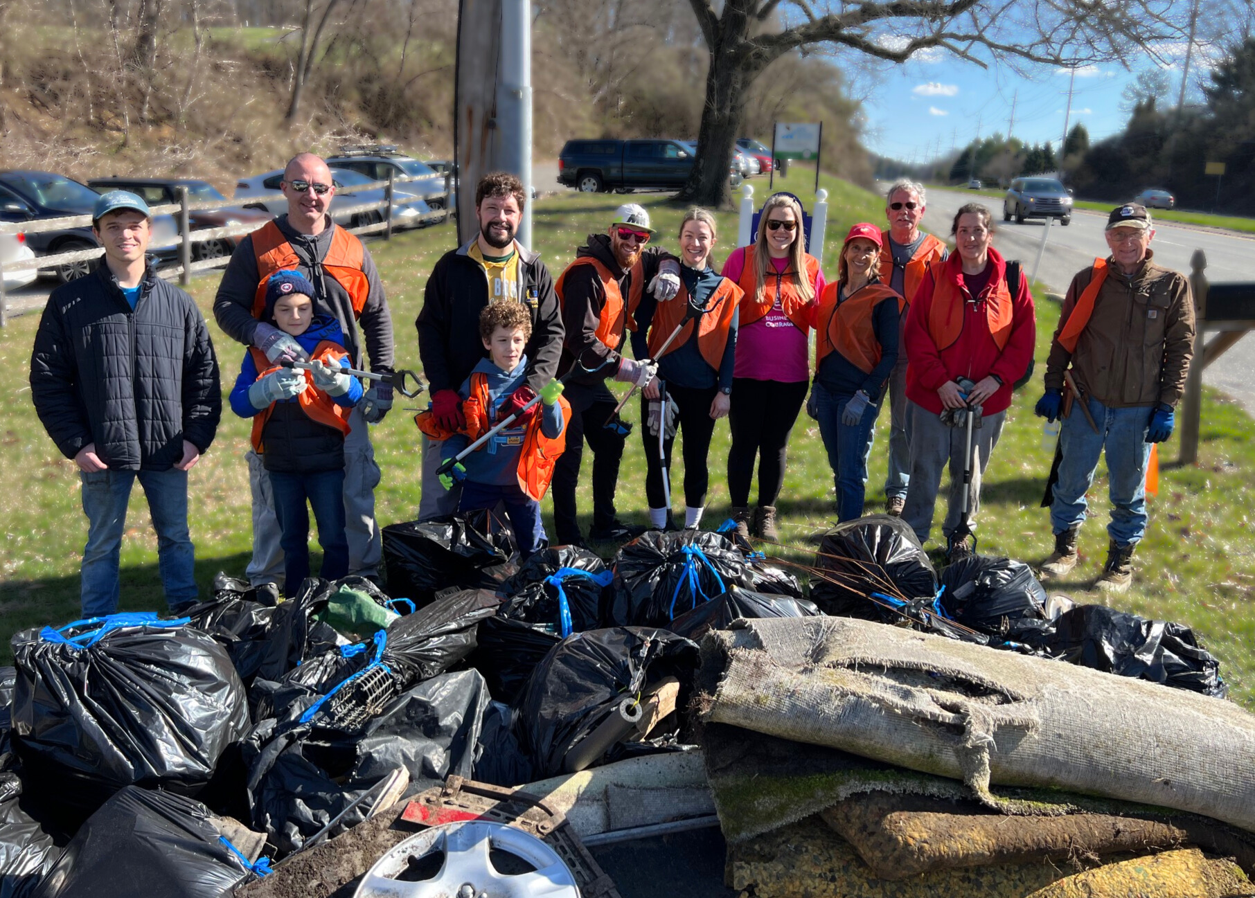 12 volunteers posing behind their trash pile, collected from near the stream on 3/16/2024