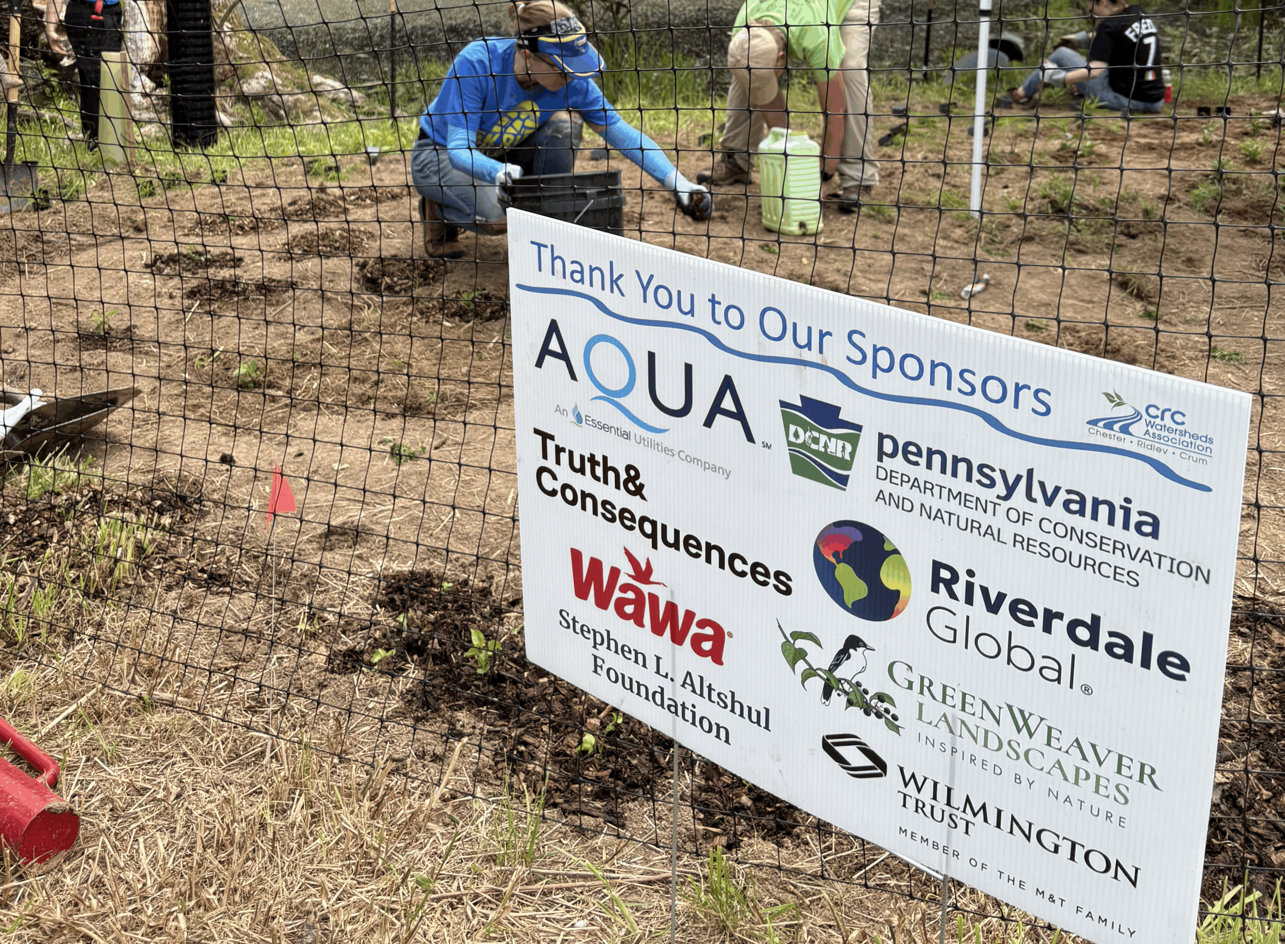Picture of sponsor sign with volunteers in the background
